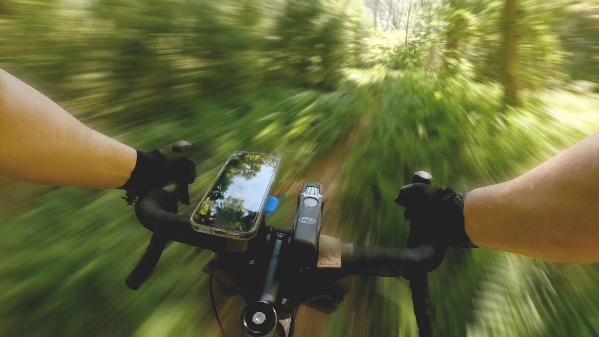 A first person point of view of hands on bicycle handlebars riding through blurry forest